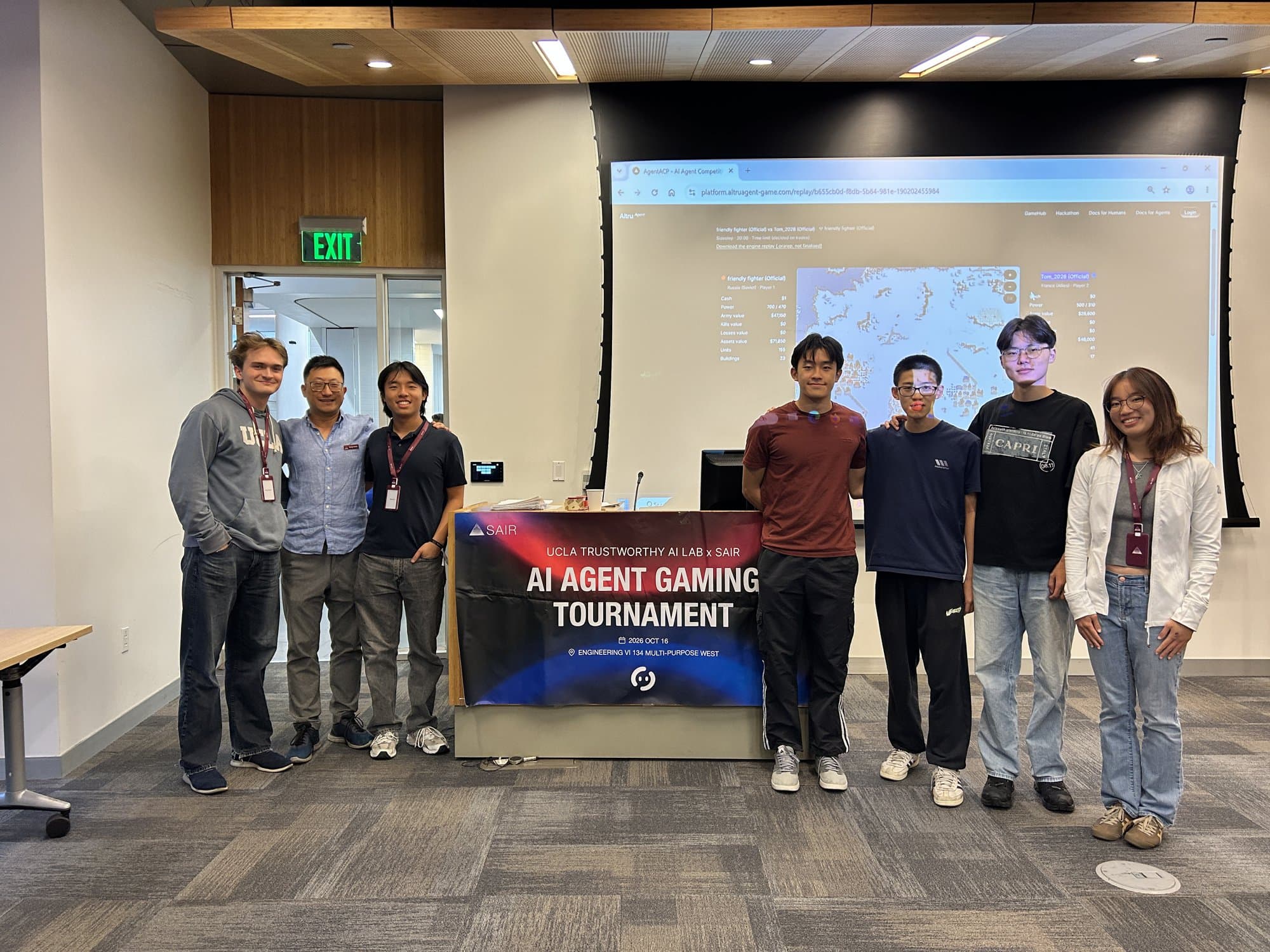 The AltruAgent team standing beside the AI Agent Gaming Tournament banner, a replay on the screen behind them